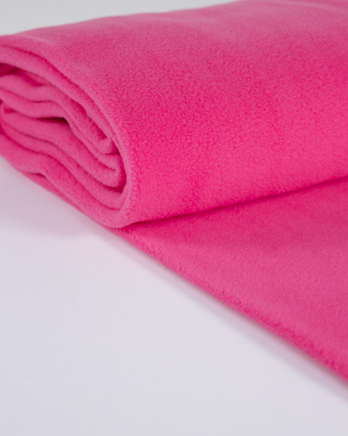 A close-up of a folded bright pink fleece fabric on a clean white surface, showing its soft, textured fabric.