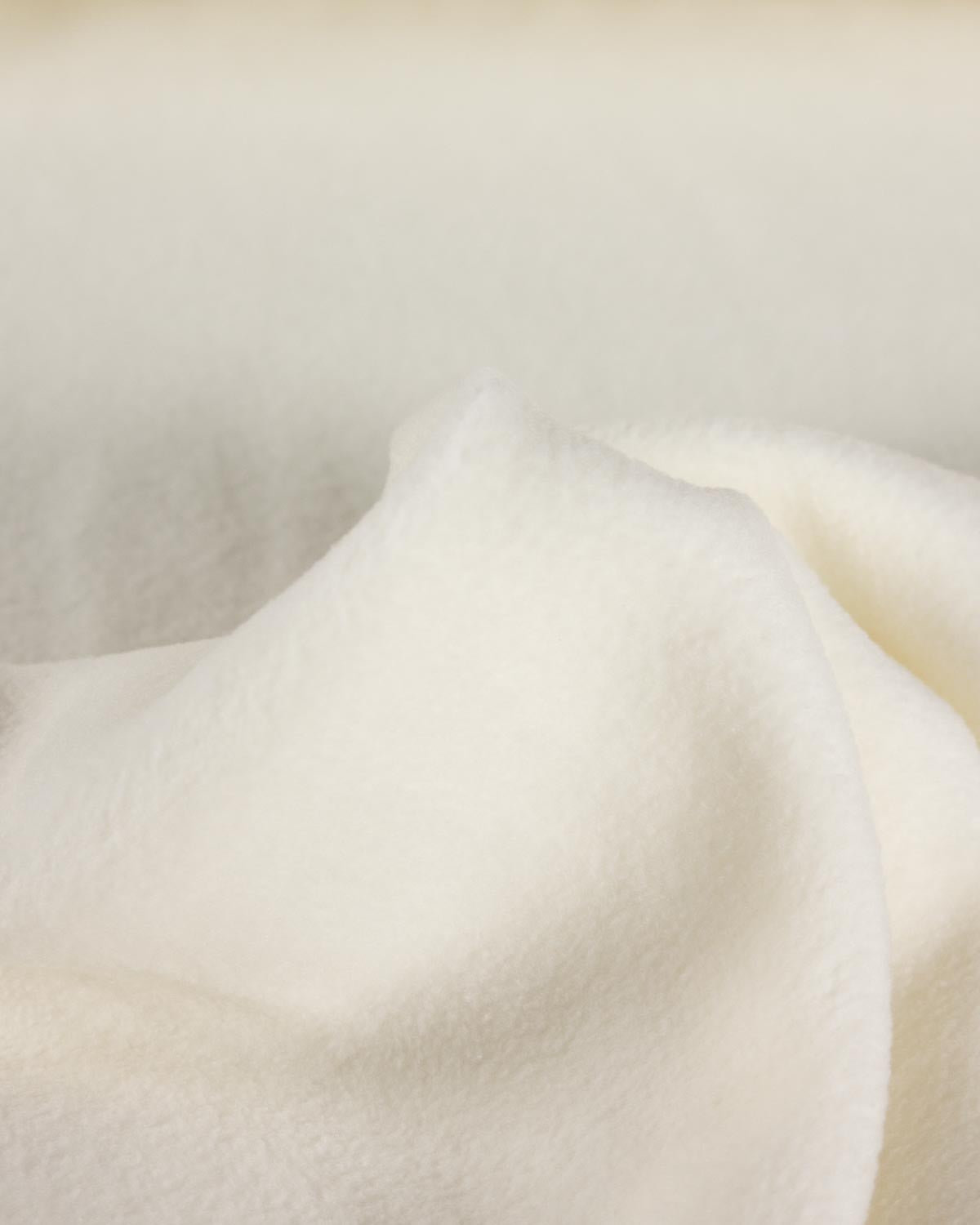 A close-up of soft, plush cream-colored fleece fabric with gentle folds and a smooth texture.