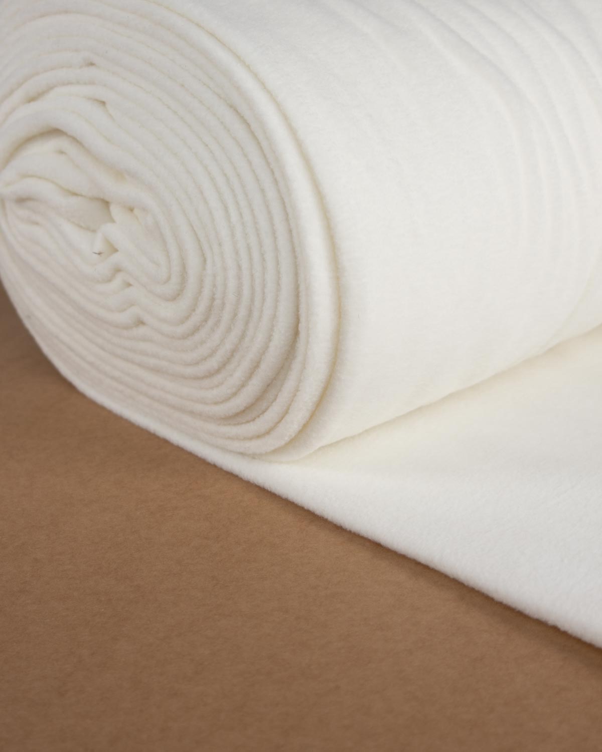 A close-up of a rolled off-white fleece fabric, showing its soft, textured surface, resting on a brown surface.