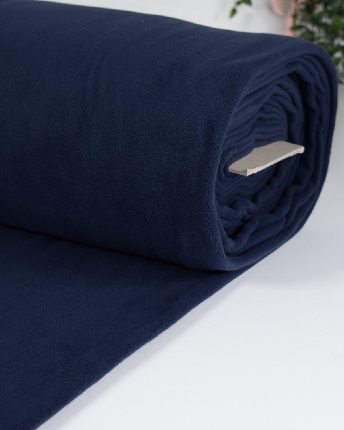 A close-up of a rolled navy blue  fleece fabric  partially unrolled, with a small white tag visible on the rolled edge against a light background.