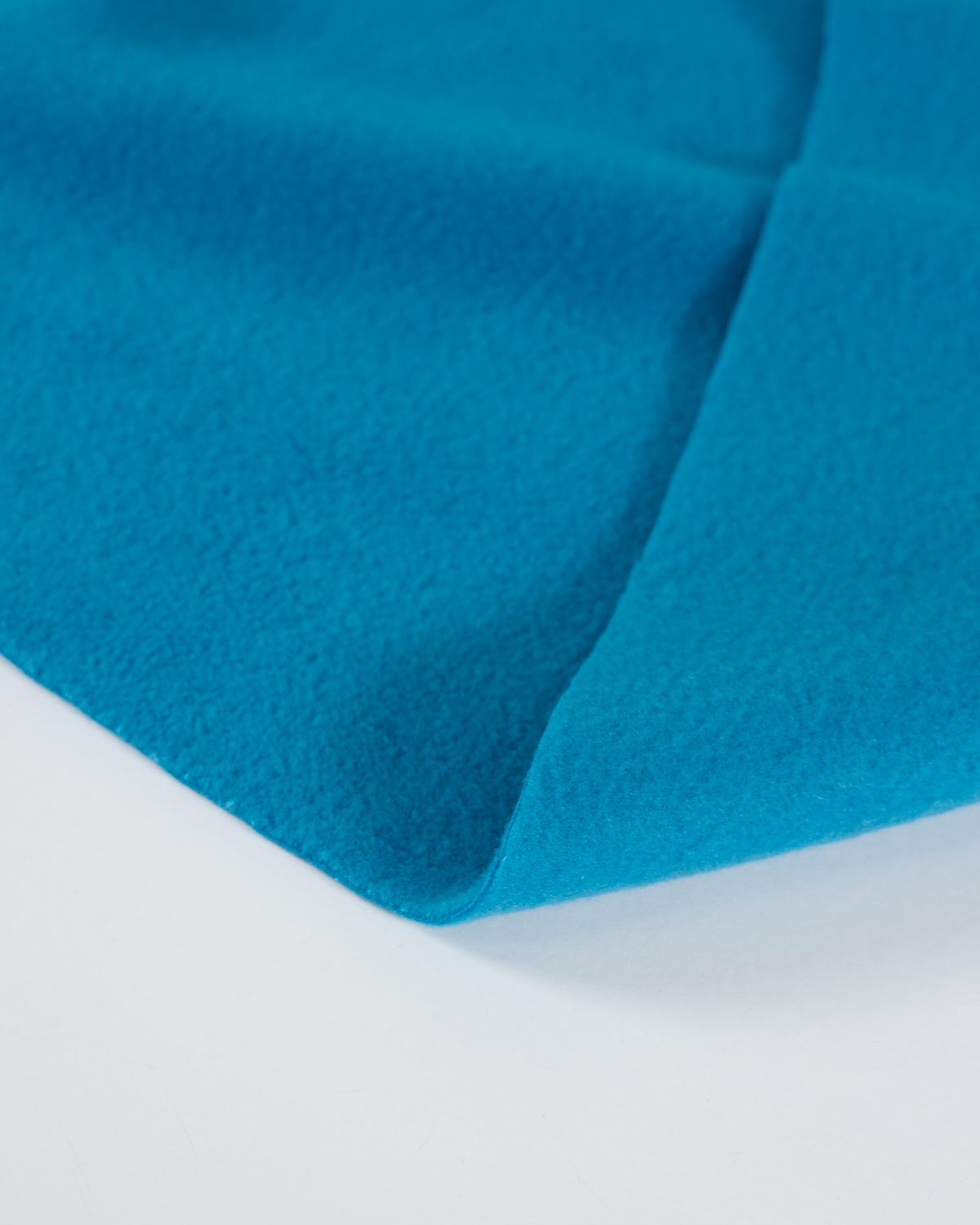 A close-up of a folded bright turquoise blue fabric, showing its soft texture and matte finish against a clean white background.