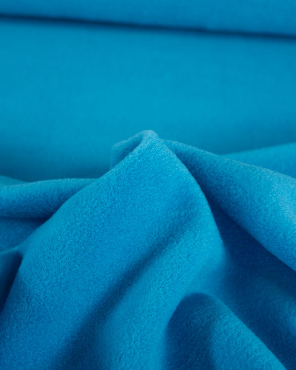A close-up of bright blue turquoise fleece fabric with soft folds and a plush texture.