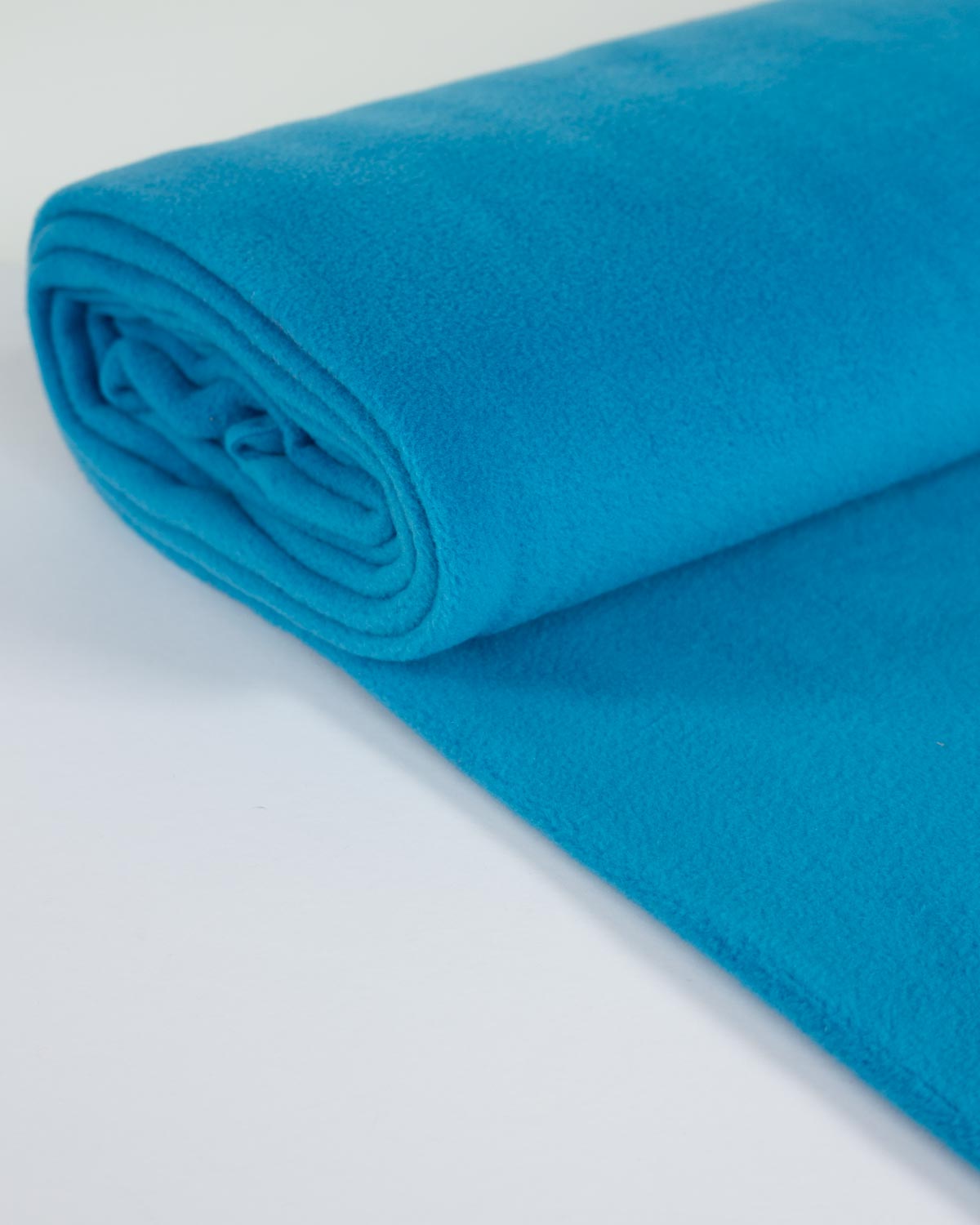A bright turquoise blue fleece fabric rolled at one end and laid out on a clean white surface.