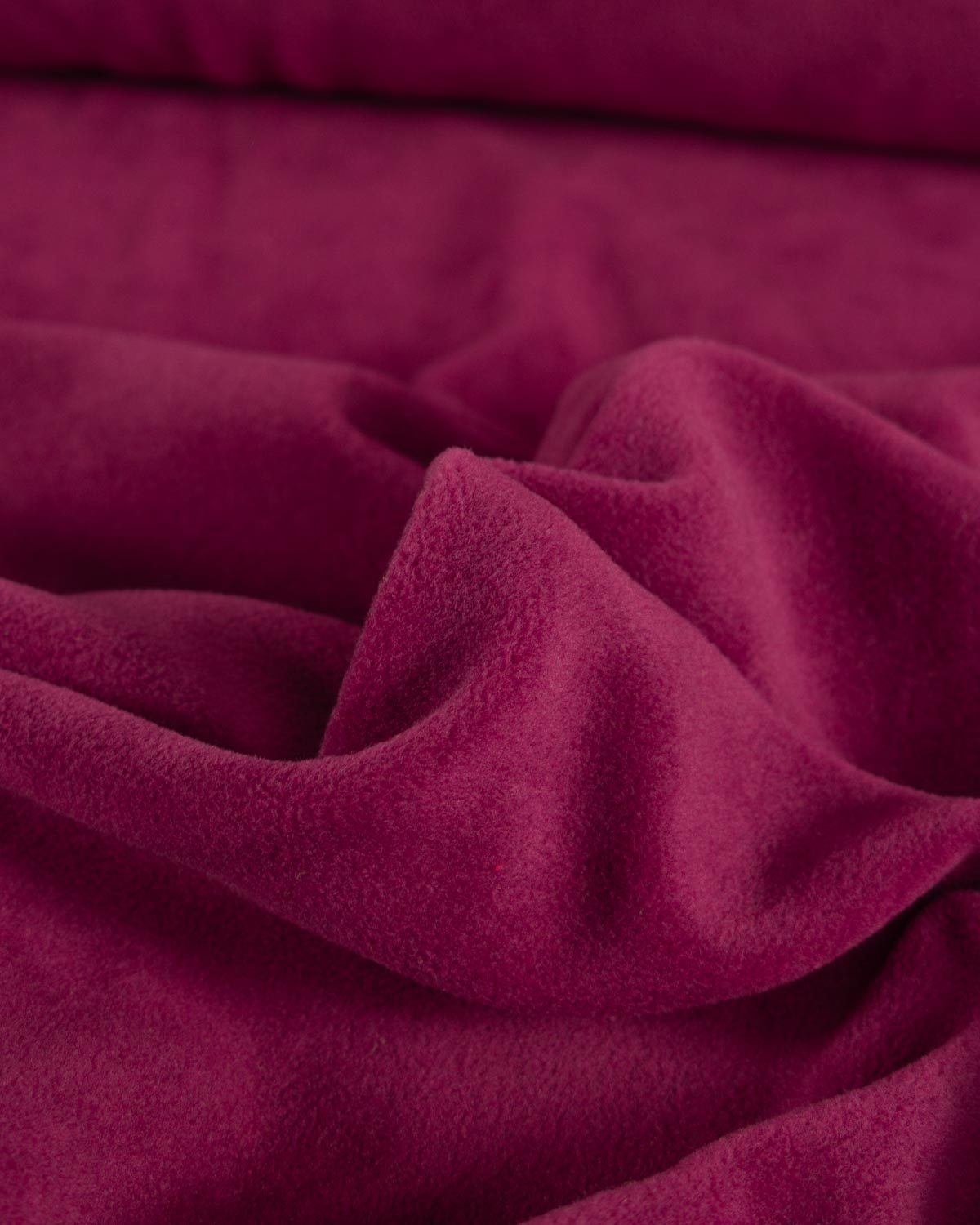 A close-up of draped plush fleece fabric in a rich wine red colour, showing the soft texture and folds.