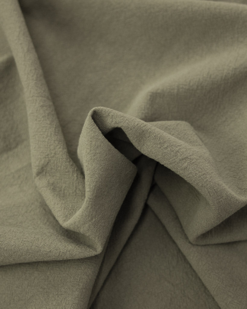 Folds of crushed washed cotton fabric in a soft grey-green