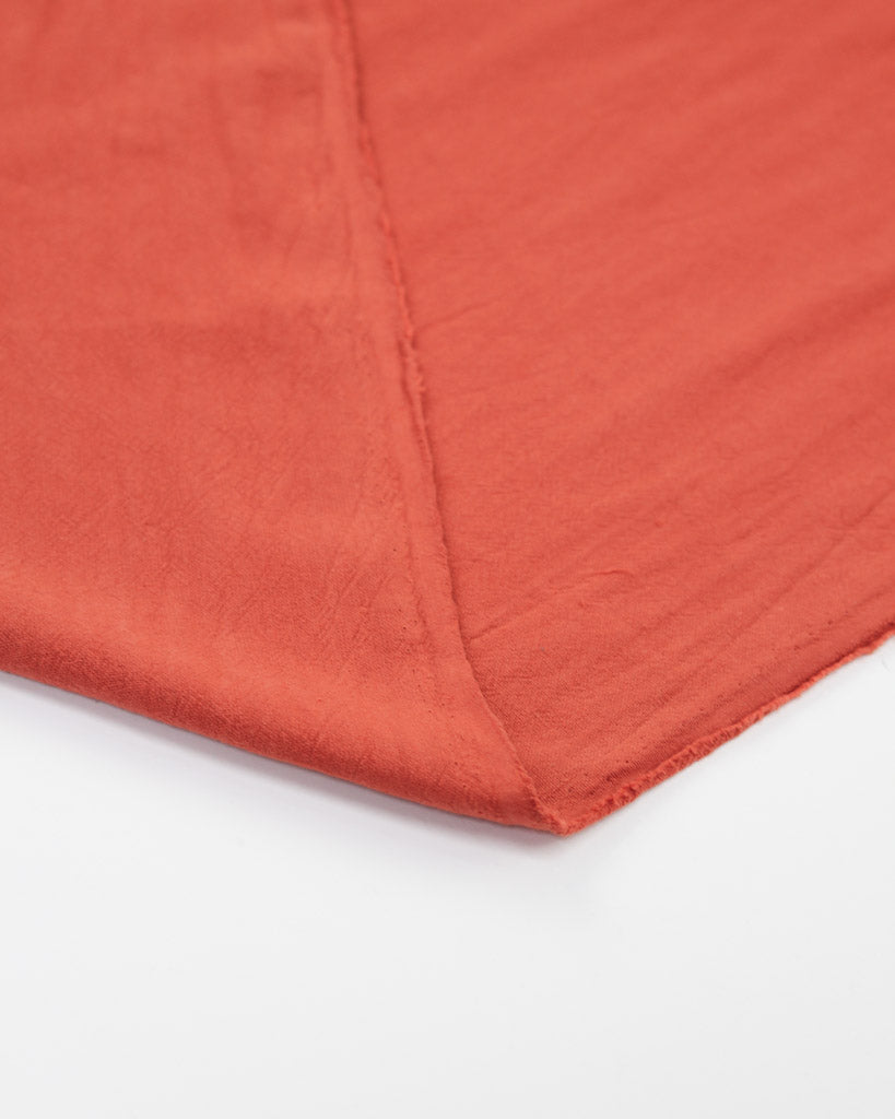 Flipped edge of crushed washed cotton fabric in hot red-orange