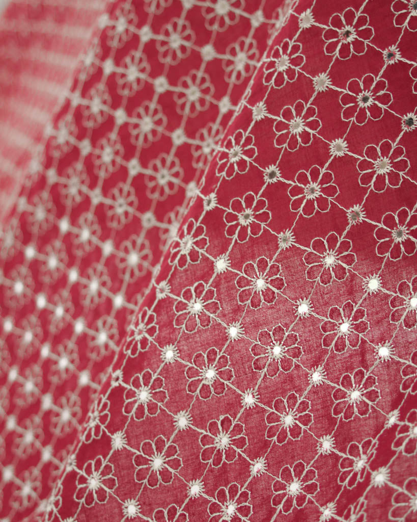 Close-up of red cotton broderie anglais fabric with white floral eyelet embroidery