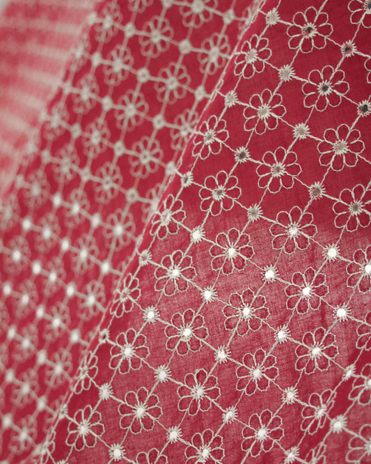 Close-up of red cotton broderie anglais fabric with white floral eyelet embroidery