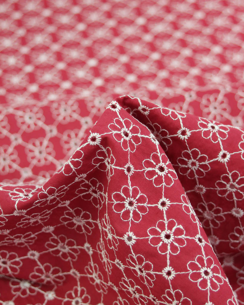 Close-up of red cotton broderie anglais fabric with white floral eyelet embroidery