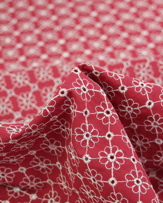 Close-up of red cotton broderie anglais fabric with white floral eyelet embroidery