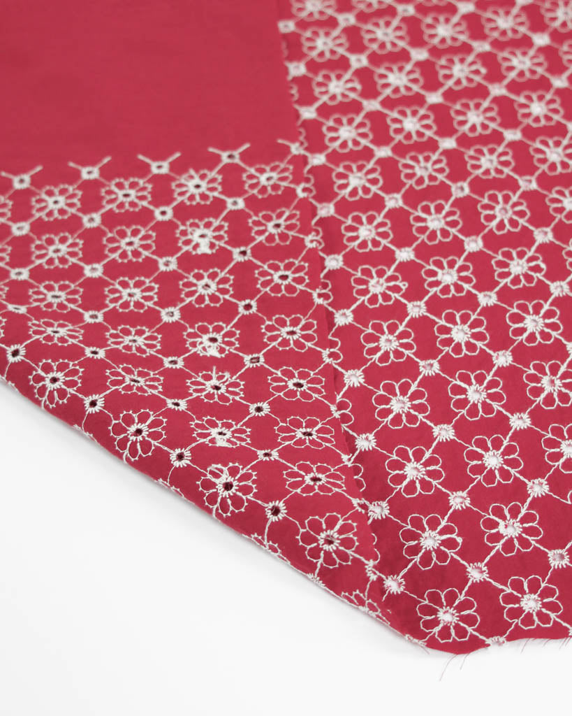 Close-up of red cotton broderie anglais fabric with white floral eyelet embroidery