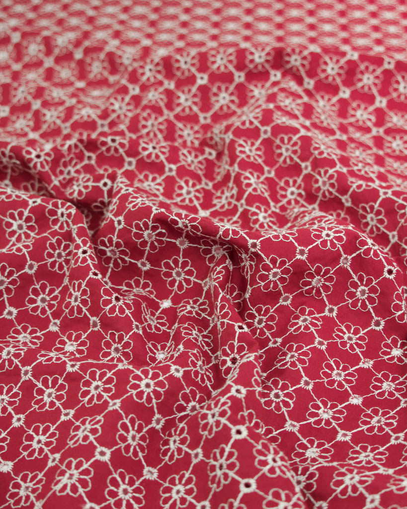 Close-up of red cotton broderie anglais fabric with white floral eyelet embroidery