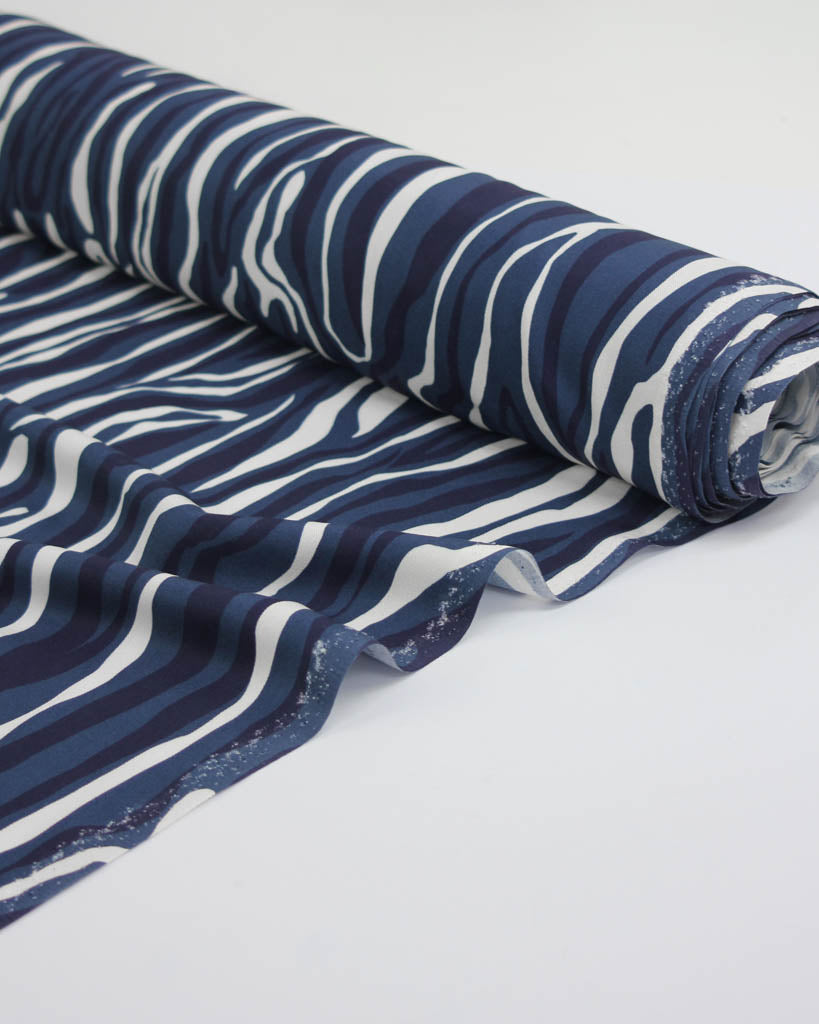 Roll of blue and white irregular striped viscose twill fabric on a white background