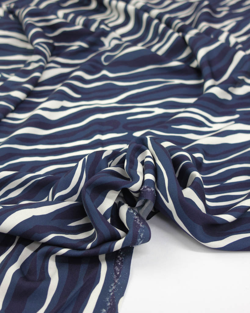 Close up of drapey viscose twill fabric with irregular navy blue and white line stripes