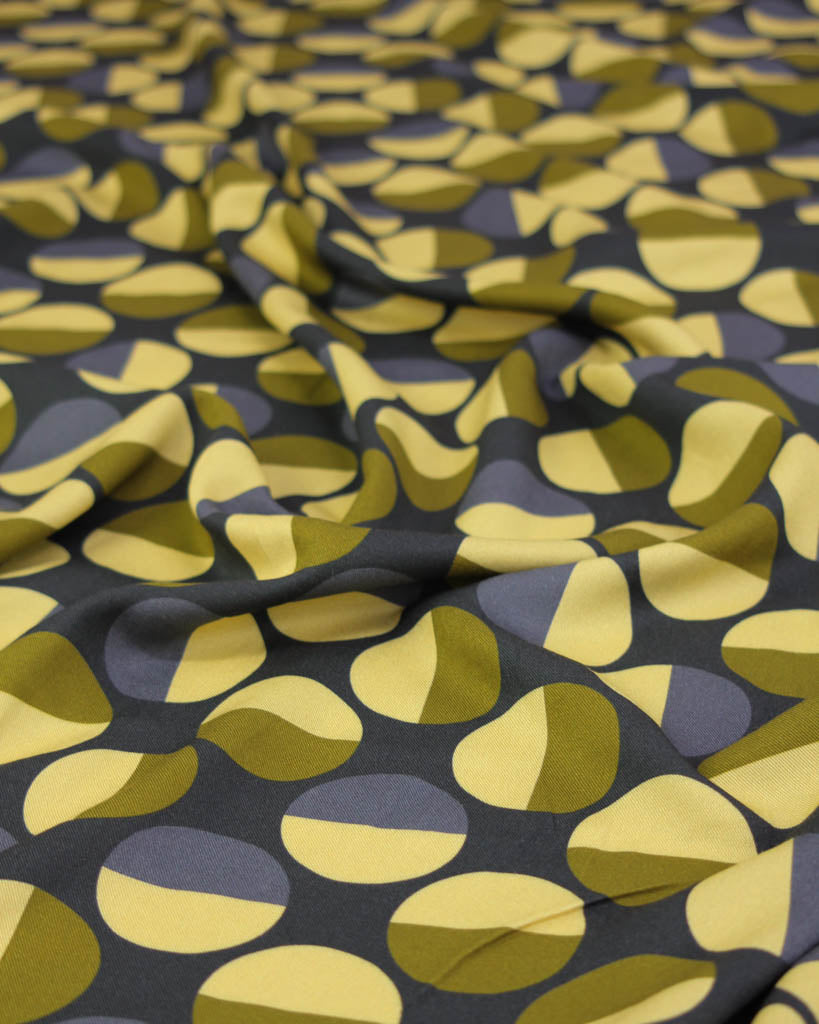 Close-up of viscose twill fabric with a pattern of yellow and green circle shapes on a dark background