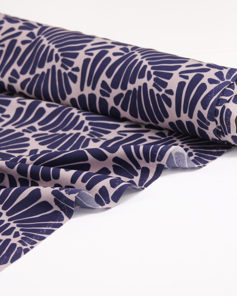 Viscose twill fabric on a roll featuring an all-over palm fan motif in deep, rich purple on a soft dusty mauve ground.