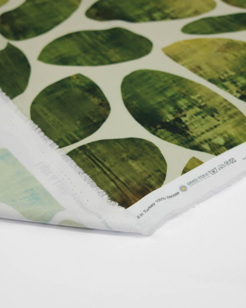 Close-up of green leaf-patterned viscose twill fabric with a white border.