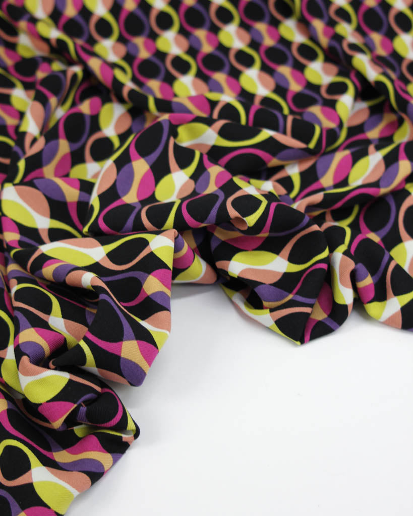 Close up of colourful abstract patterned viscose twill fabric in pink, yellow and purple on a black background
