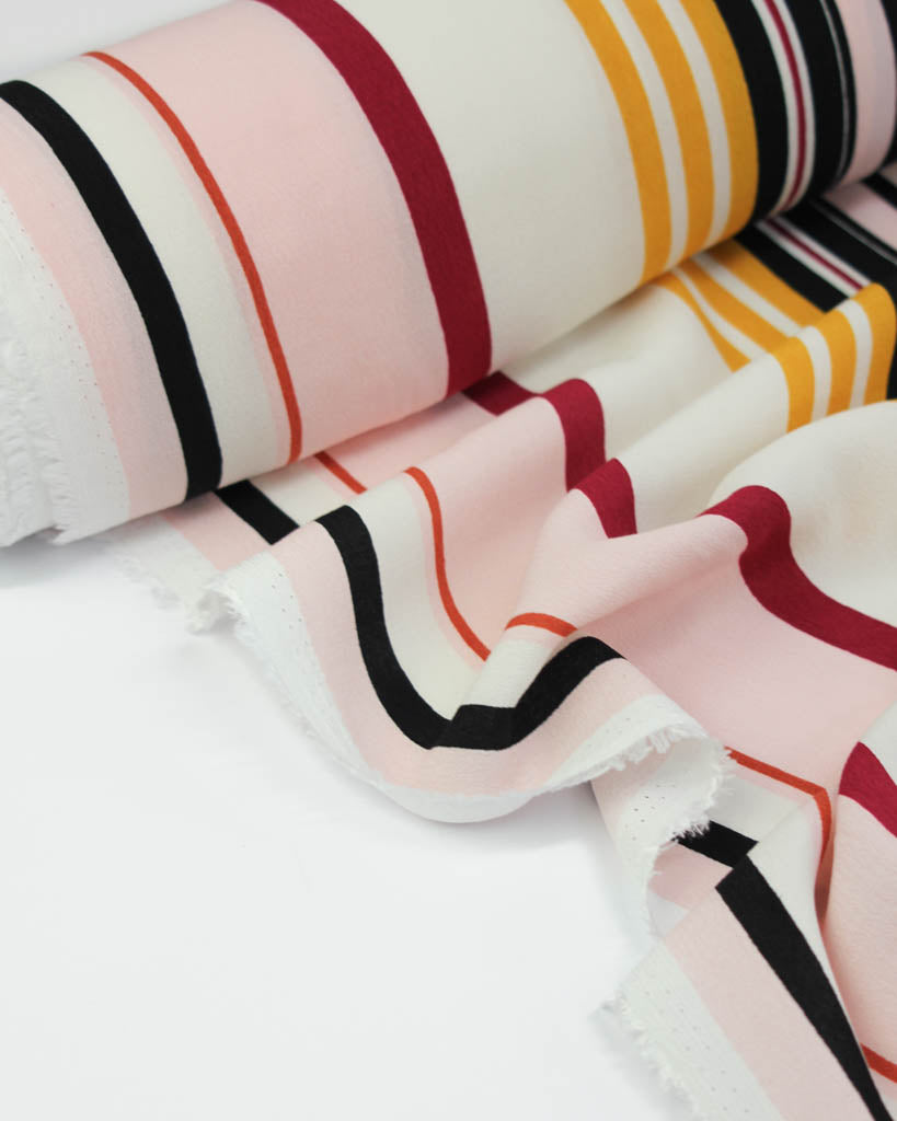 Close-up of striped viscose crepe fabric with pink, red, black, and yellow colors on a white background.