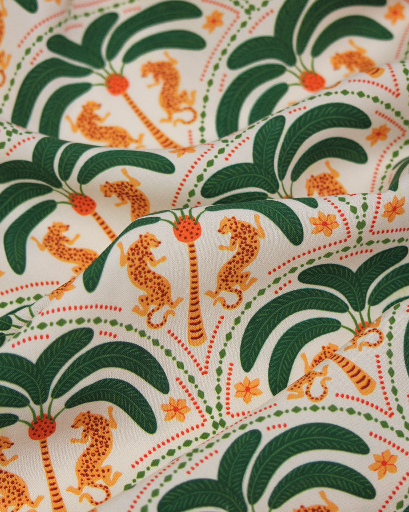 Patterned viscose fabric with orange leopards and green palm trees on a white background