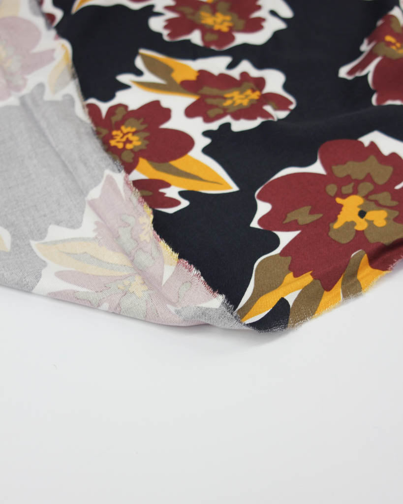 Floral viscose fabric with red and yellow flowers on a black background, folded over gray fabric.