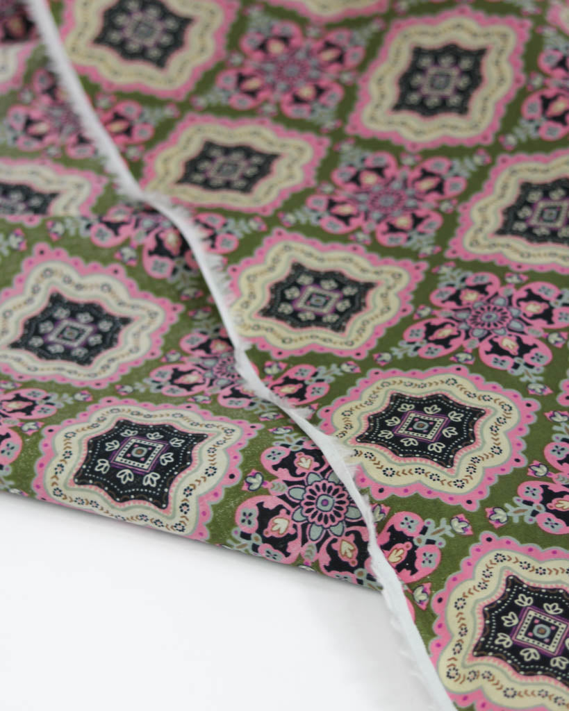 Close-up of patterned cotton lawn fabric with green, pink, and black tile design on a white background