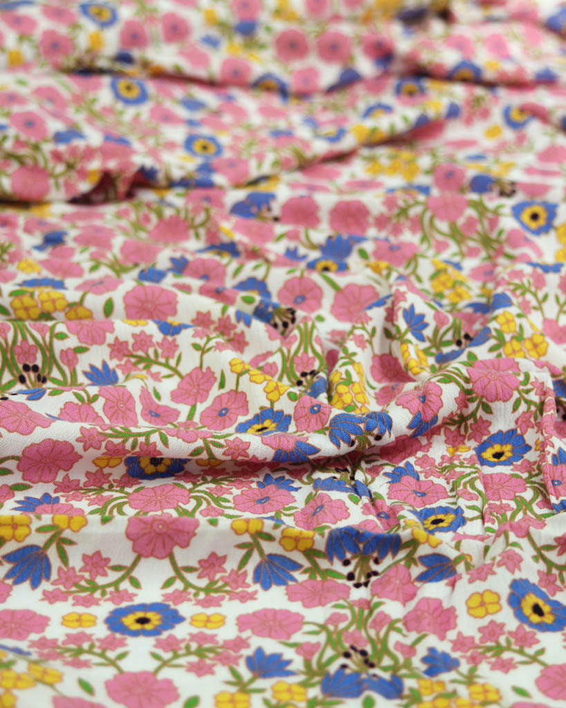 Close-up of colourful pink floral viscose crepe fabric with pink, blue, yellow, and green flowers.