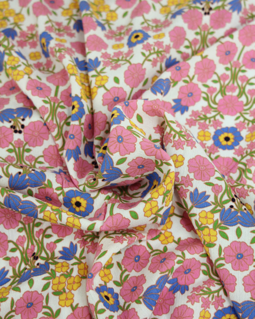 Colourful floral viscose crepe fabric with pink, blue, yellow, and green flowers on a white background.