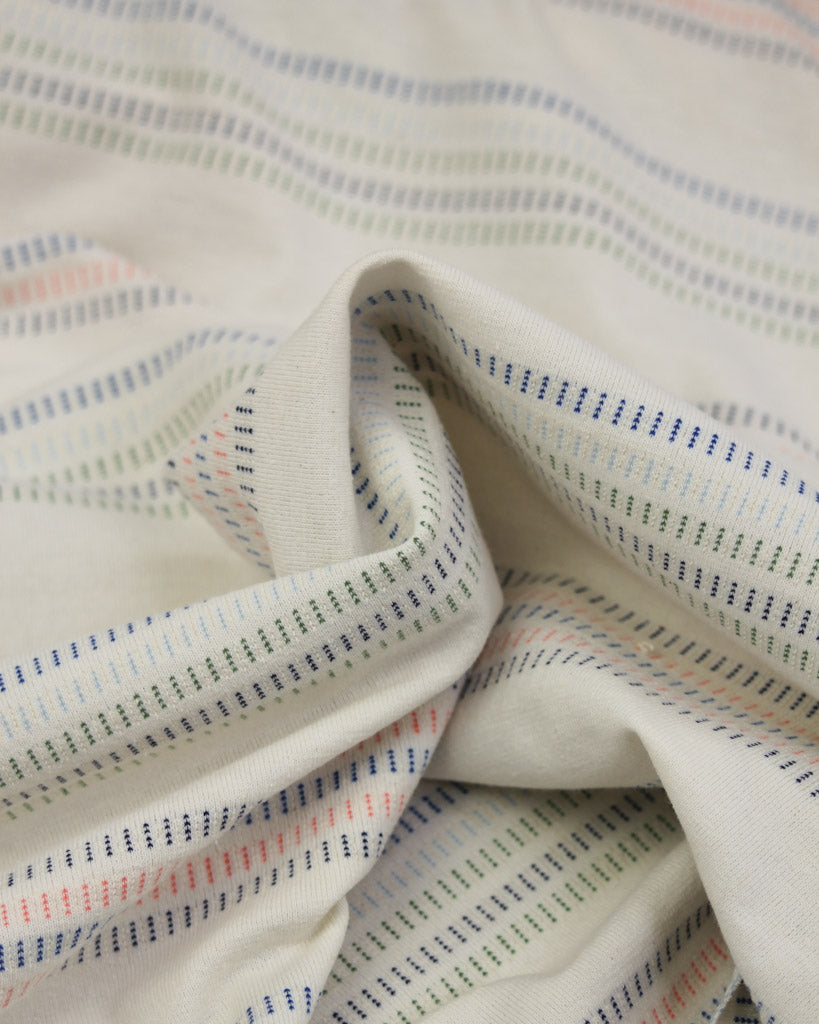 Close-up of cotton jersey fabric with a striped pattern in beige, blue, and red.