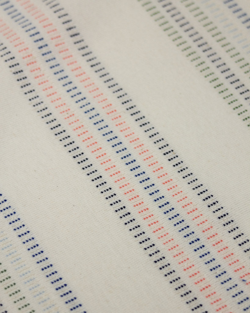 Close-up of a cotton jersey fabric with a pattern of small, evenly spaced dots in various colors on a neutral background.