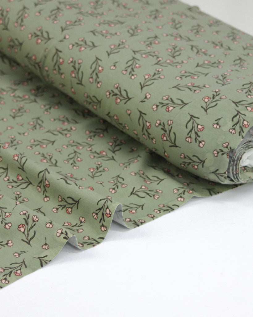 Roll of green stretch jersey fabric with small floral pattern on a white background