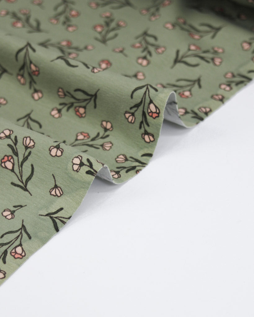 Stretch jersey knit fabric with floral pattern on a pale green background