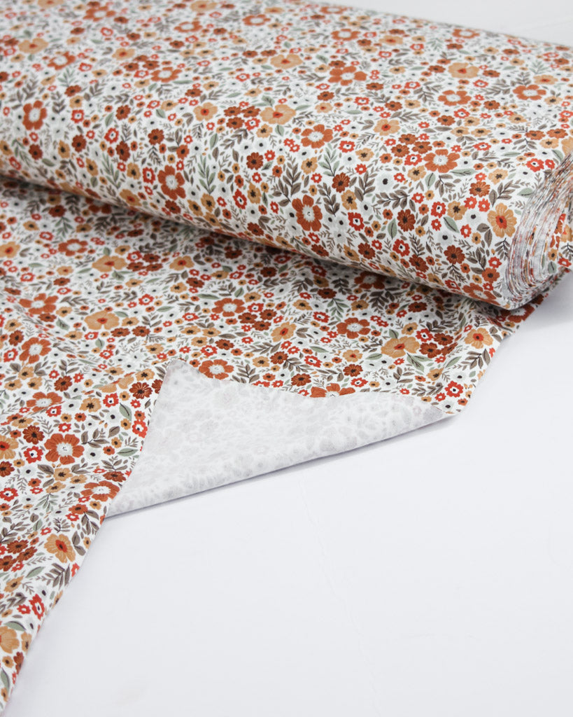 Roll of floral jersey fabric with small orange flowers on a white background
