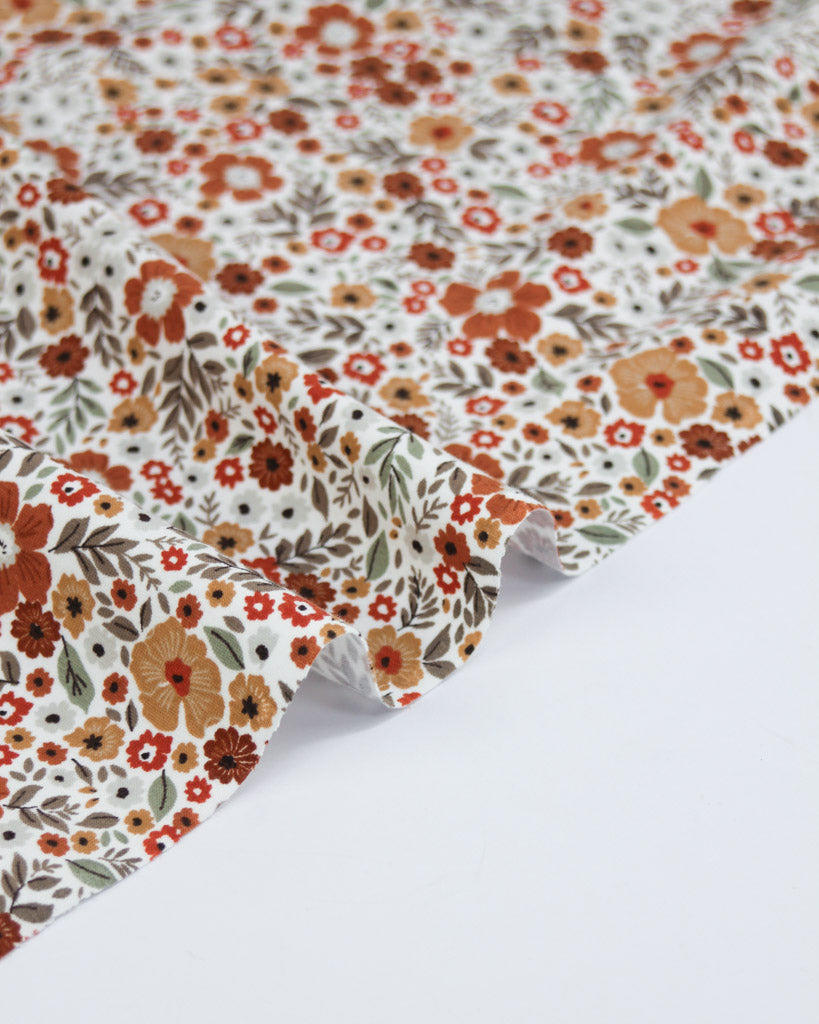 Floral patterned cotton jersey fabric with orange and red flowers on a white background