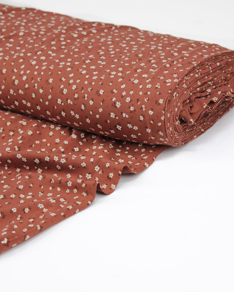 Roll of rust orange fabric with small white daisy floral pattern on a white background