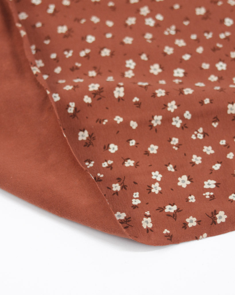 Rust orange cotton jersey fabric with small white floral pattern on a white background