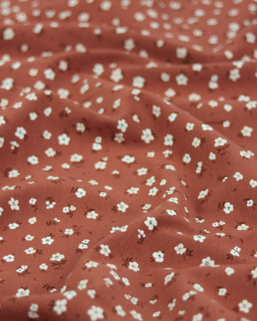 Rust orange red cotton jersey fabric with small white floral pattern