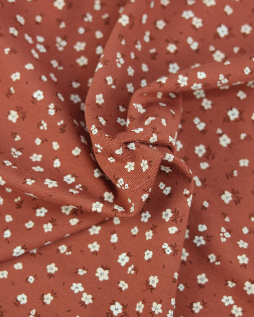 Rust orange cotton jersey fabric with small white floral pattern