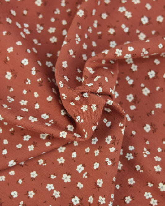 Rust orange cotton jersey fabric with small white floral pattern