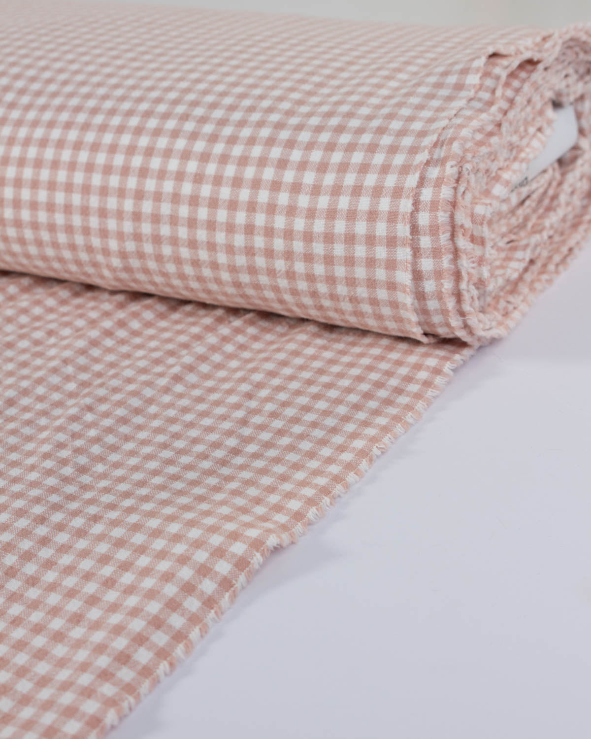 Roll of pink and white checkered gingham cotton fabric on a light gray background