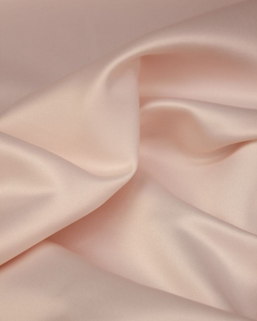 Close-up of smooth, light pink satin fabric with soft folds.