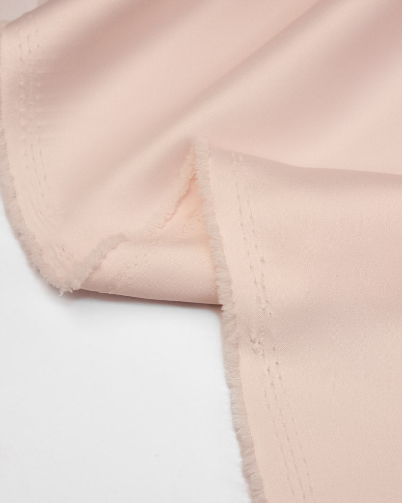 Close-up of light pink satin fabric with a white background