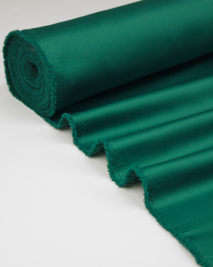 Roll of green duchess satin fabric on a white background