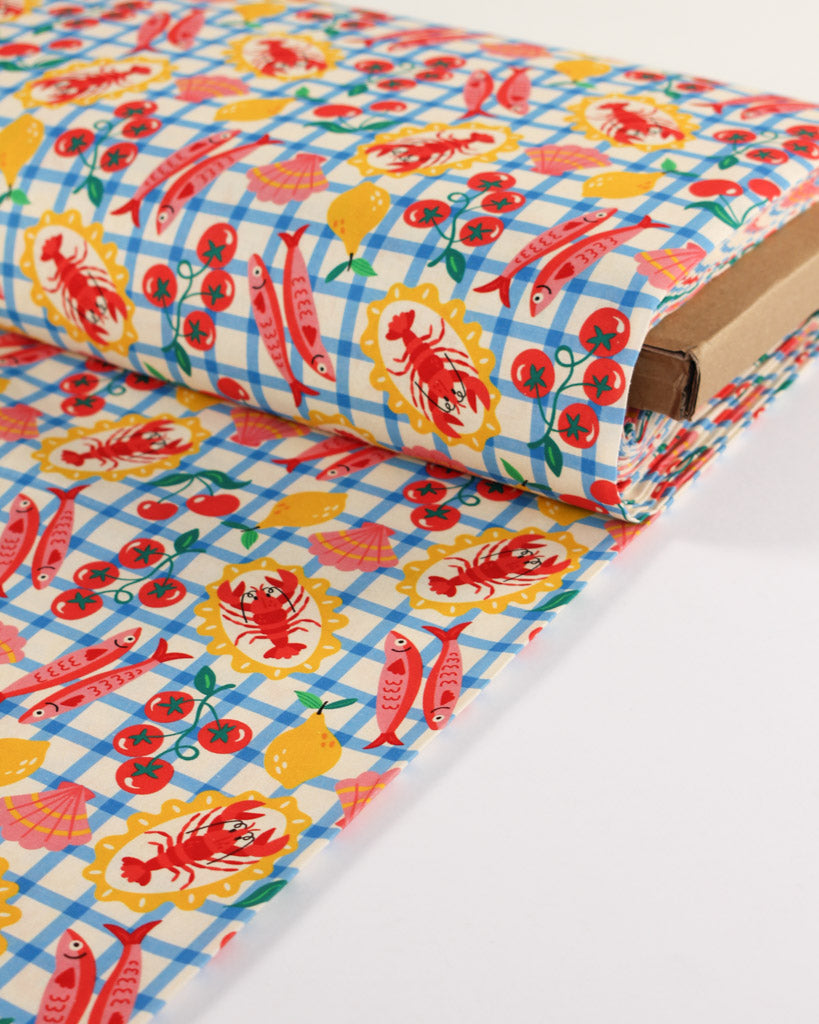 Roll of colourful cotton fabric with fish and lobster design on a blue checkered white background