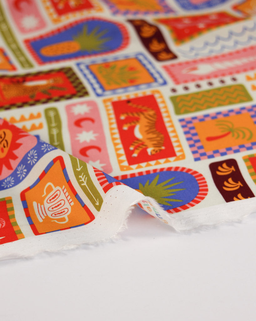 Colourful viscose fabric with patterned holiday stamp design on a white background featuring illustrations of tigers, seashells, suns, palm trees, fruit, pineapples, bananas and tropical imagery