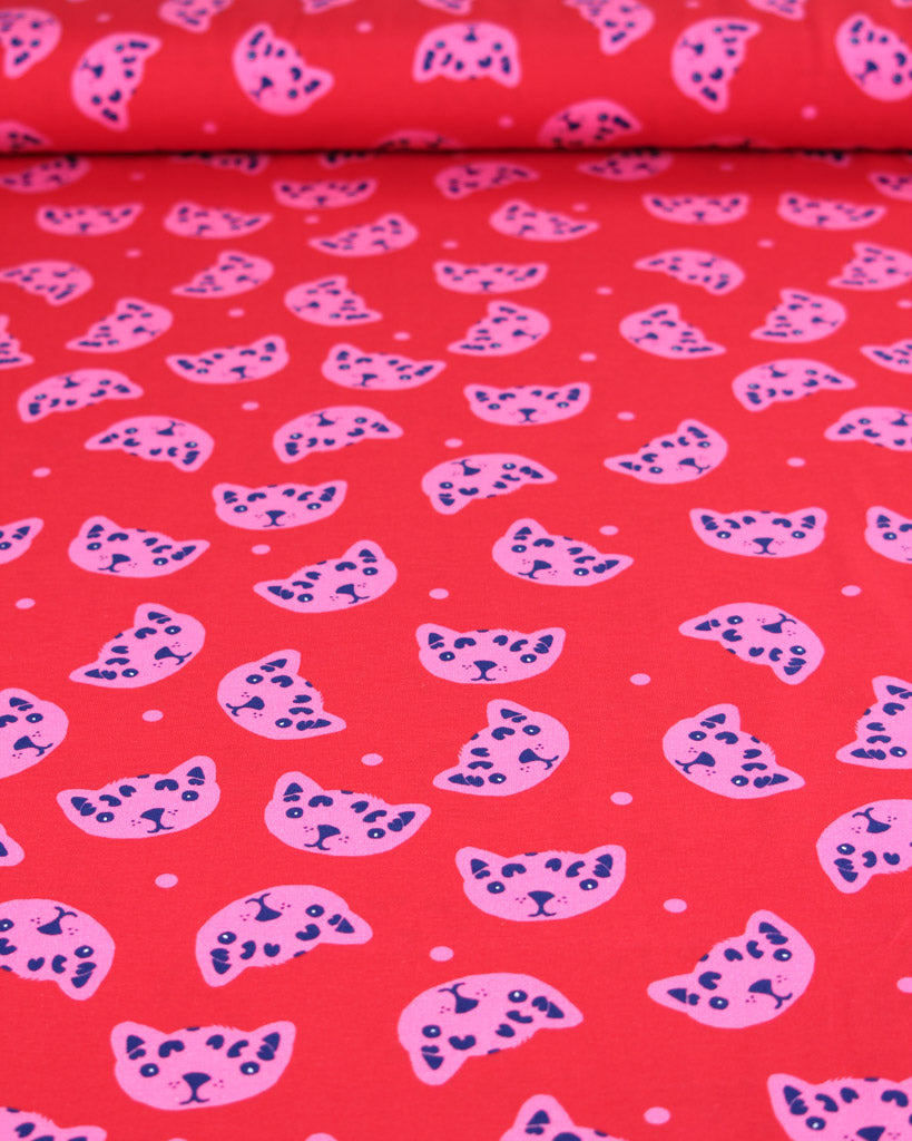Cotton jersey fabric with pink and blue cat pattern on a red background