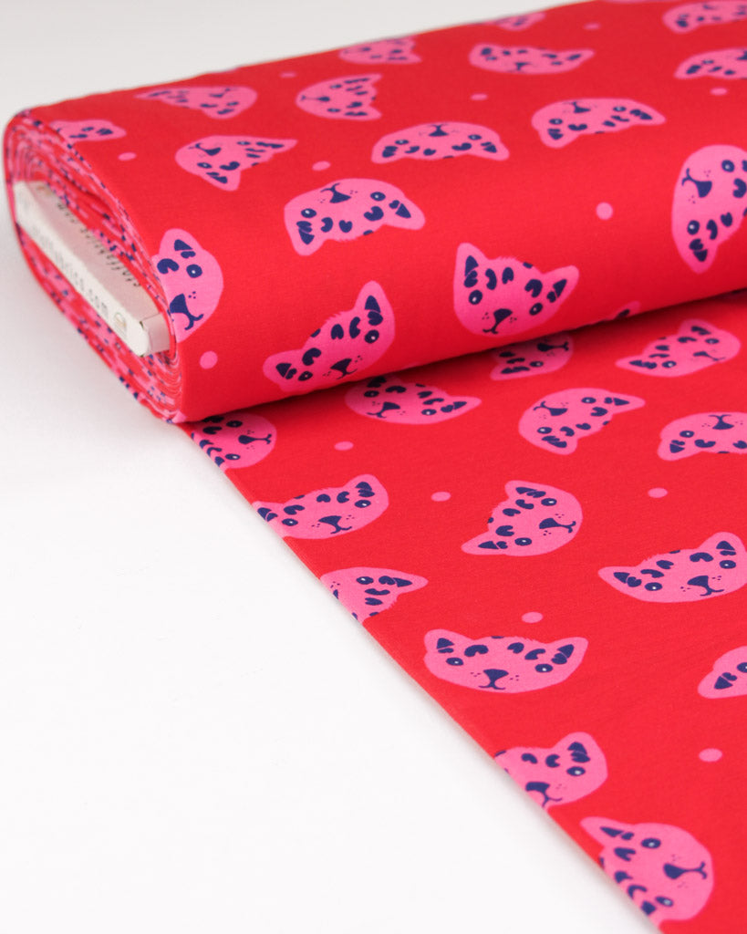 Roll of red cotton jersey fabric with pink cat pattern on a white background
