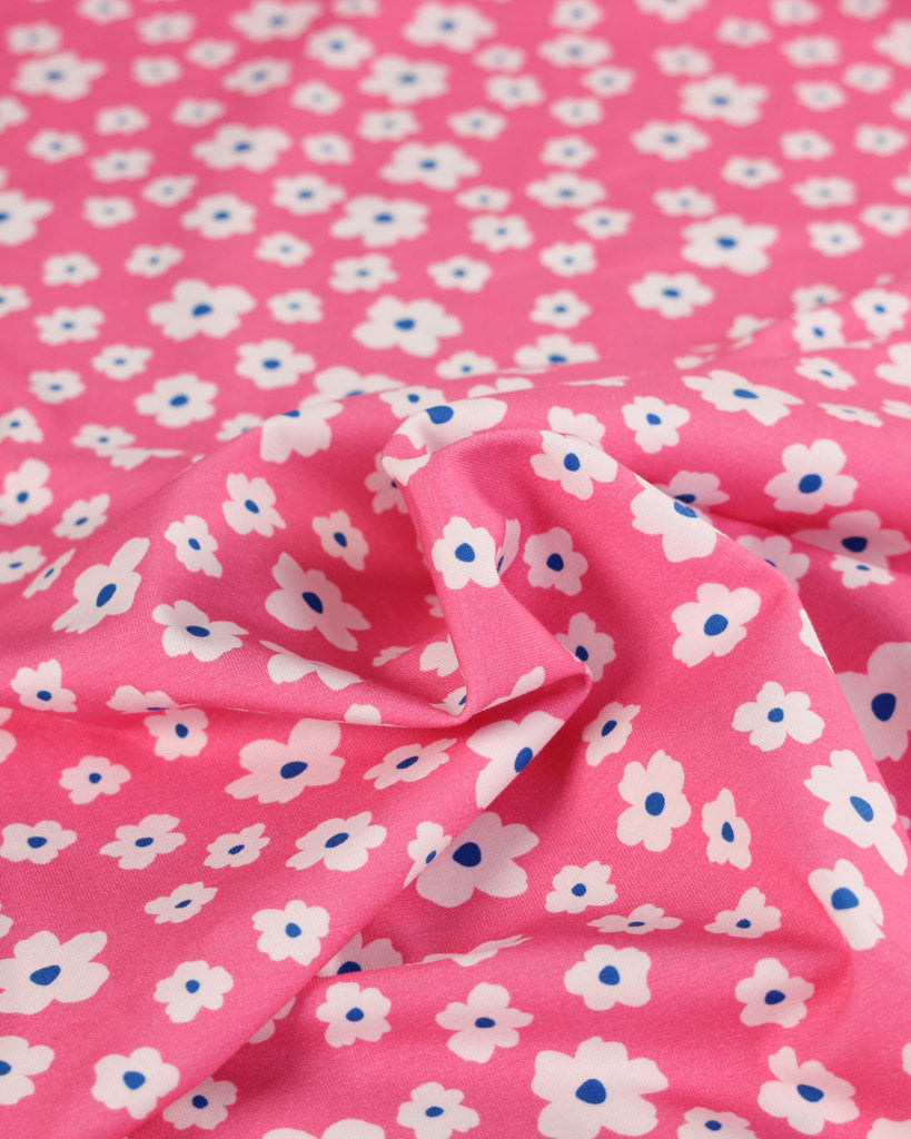 Pink cotton jersey fabric with a print of small white flowers and blue centers