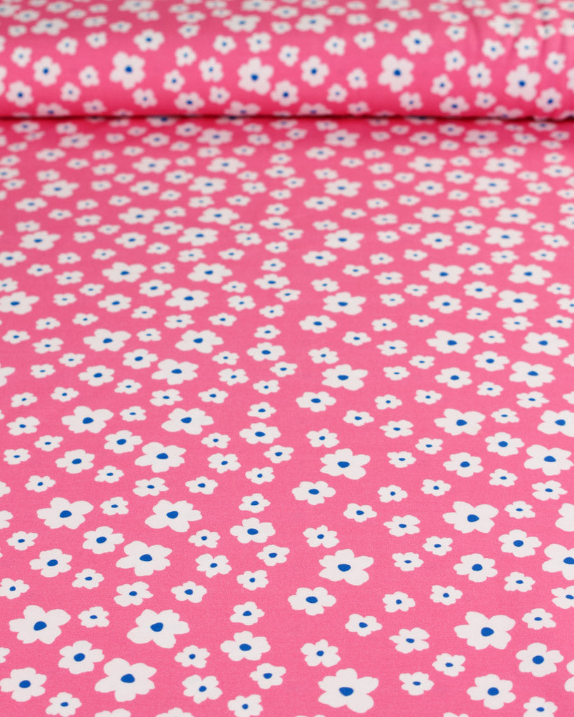 Pink fabric with small white flowers and blue centers on stretchy cotton jersey fabric