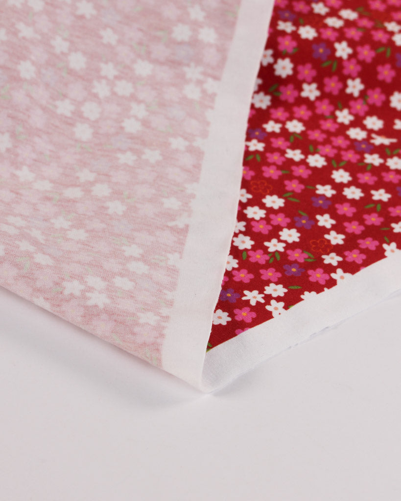 Reverse of floral-patterned cotton jersey fabric, one pink with white flowers and the other red with multicoloured flowers, on a white background.